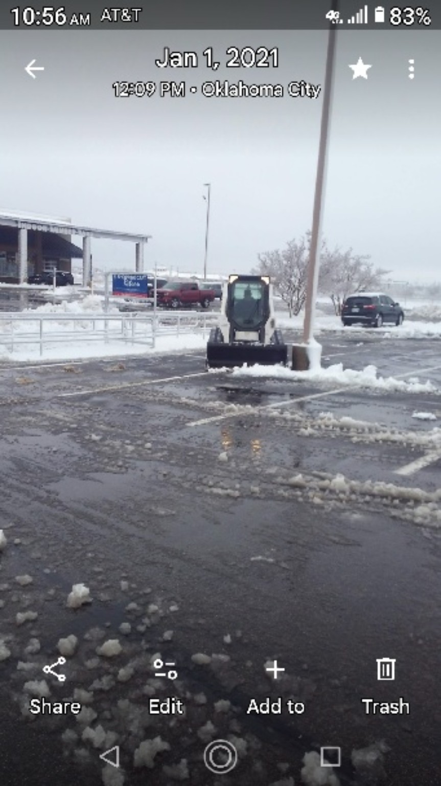 A skid-steer clears snow from a commercial parking lot.